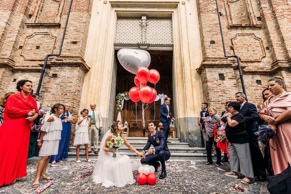 Wedding celebration outside church entrance with red and white balloons and gathered guests.