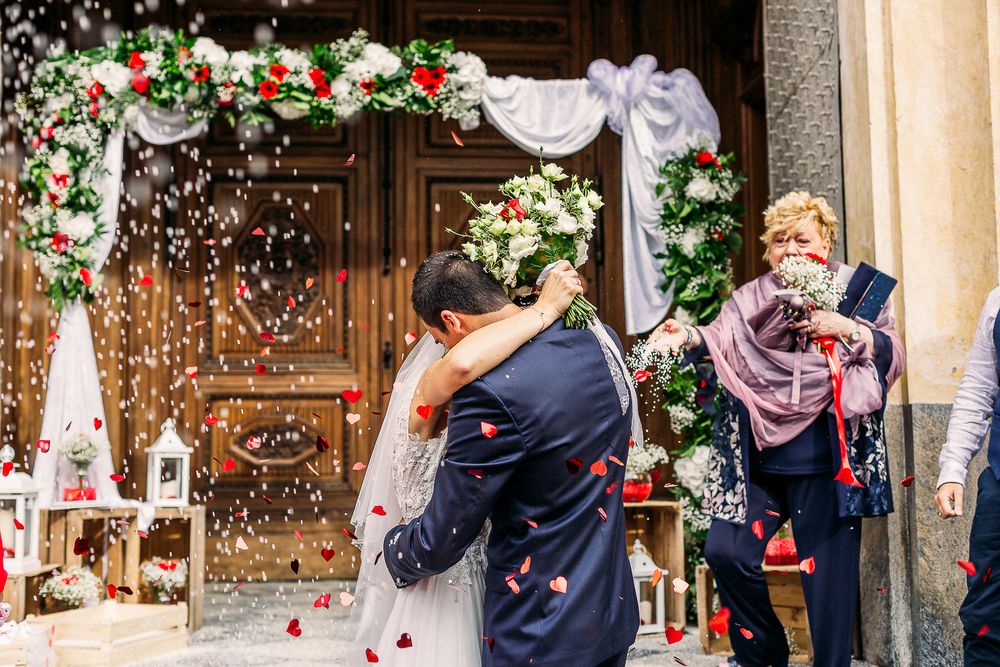 Newlyweds celebrate under floral arch as guests throw confetti during exit.