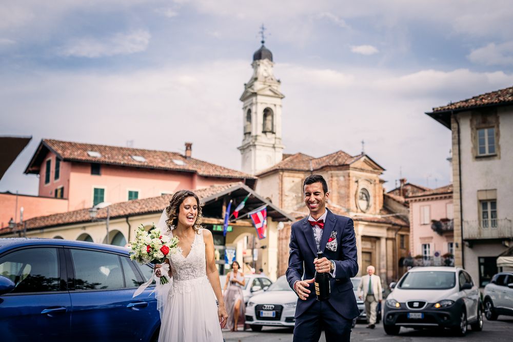Wedding couple walking in Italian village street with church bell tower in background.