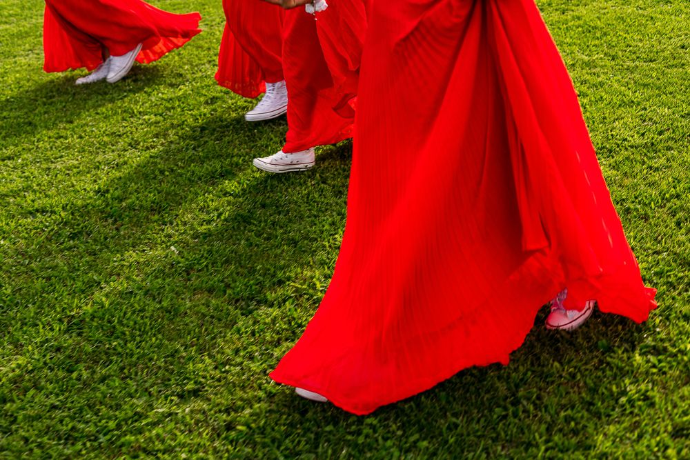Red bridesmaid dresses and white shoes elegantly displayed on vibrant green grass at an outdoor wedding.