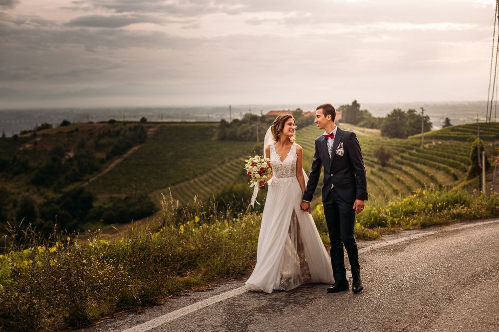 Newlyweds walking hand in hand along a countryside path with rolling hills in background.
