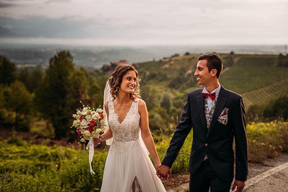Happy couple walking along vineyard path carrying beautiful wedding bouquet.