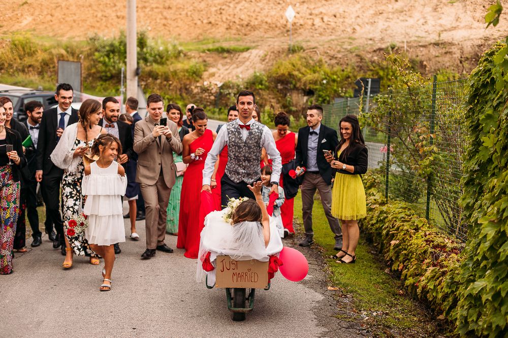 Wedding celebration procession with guests and a scooter on a garden path.