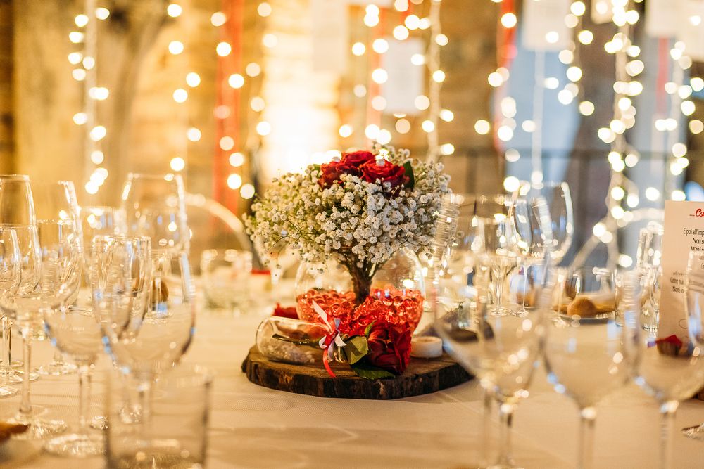 Wedding table centerpiece with baby's breath flowers and red accents surrounded by wine glasses.