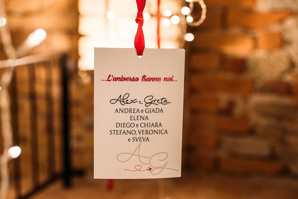 Elegant wedding invitation card hanging from red ribbon against warm blurred background.