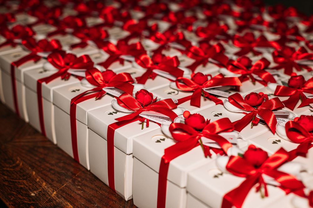 Rows of white wedding favor boxes decorated with red bows on wooden surface.