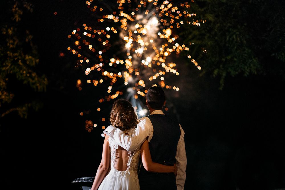 A couple watches fireworks together during their wedding celebration at night.