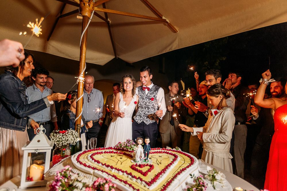Wedding guests gathering around a heart-shaped cake with sparklers at the reception.