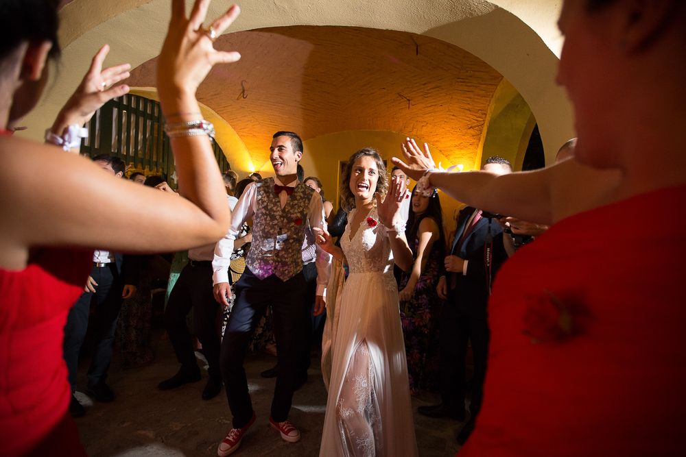 Wedding guests dancing and celebrating in an arched venue with ambient lighting.
