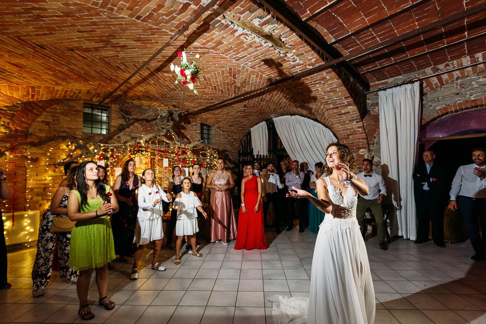 Wedding guests watch a romantic first dance in a rustic brick-walled venue decorated with twinkling lights and white drapes.