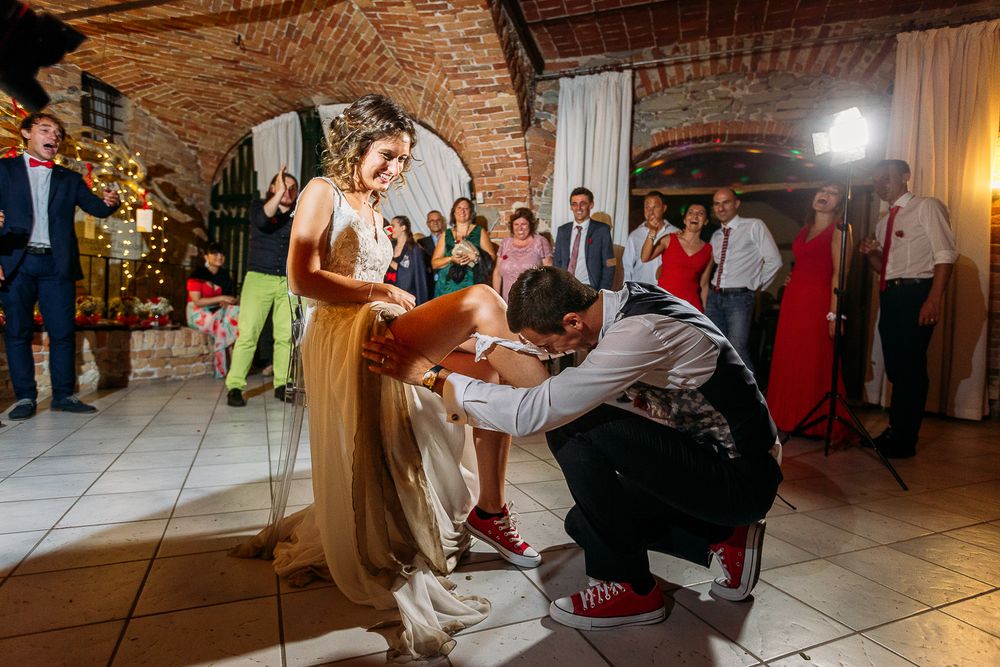 A traditional garter removal ceremony takes place on a tiled dance floor in a rustic brick venue.