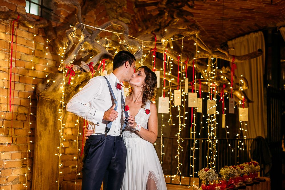 A romantic moment under twinkling fairy lights in a rustic brick-walled reception venue.