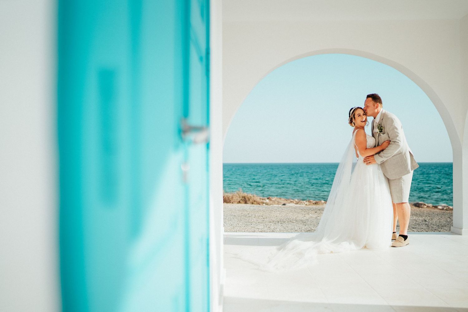 A wedding moment framed through a blue-white archway overlooking the Mediterranean Sea.