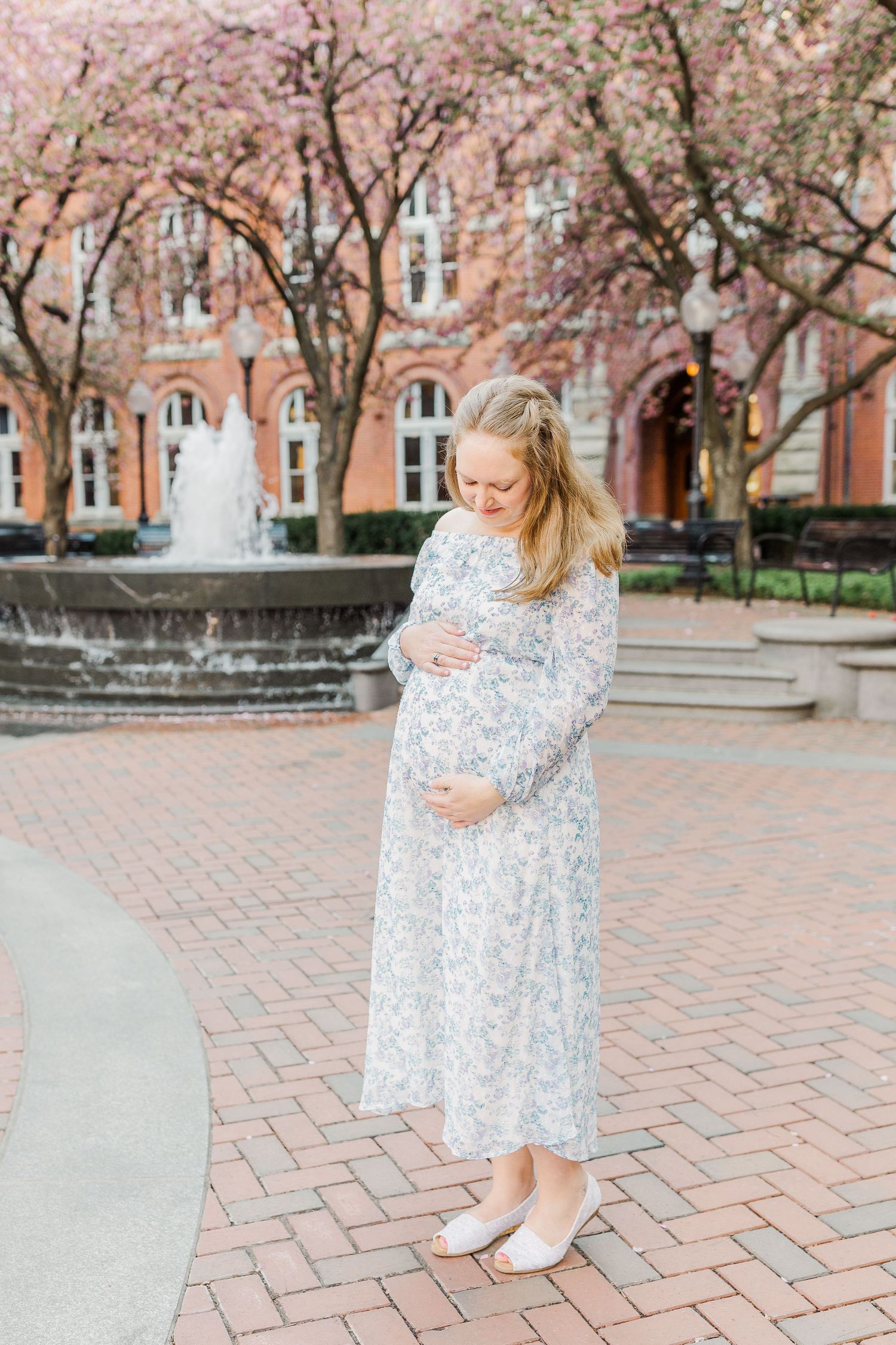 A light blue floral dress twirls against a backdrop of spring blossoms and brick architecture.
