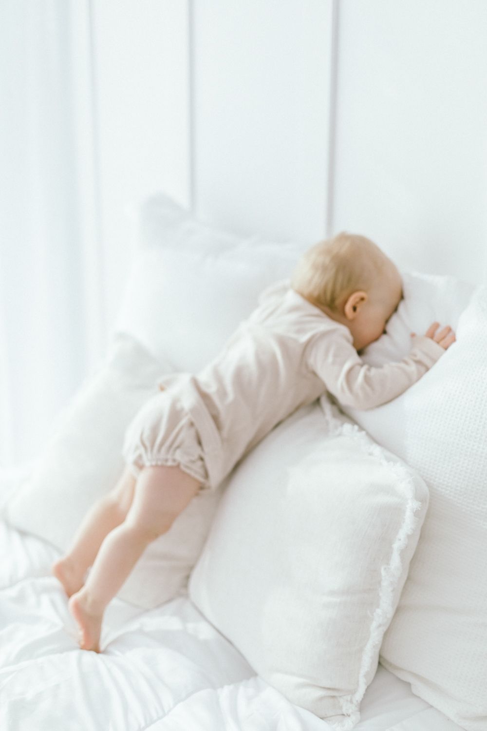 Baby in cream romper sleeping peacefully on white pillow.