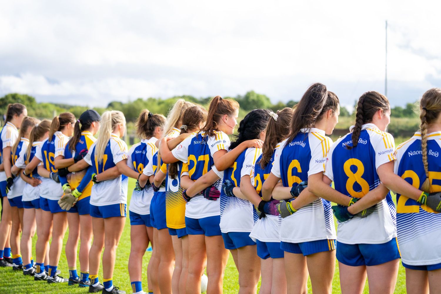 A line of athletes in blue and yellow uniforms standing together on a sports field.