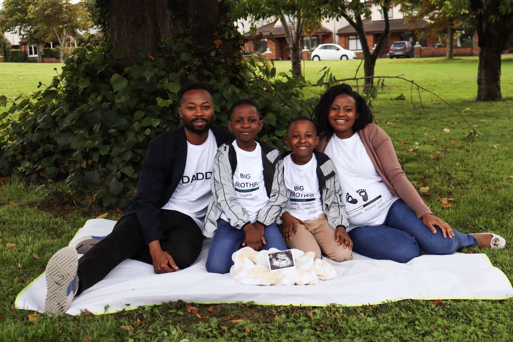 Family group sitting on white blanket outdoors wearing matching t-shirts.