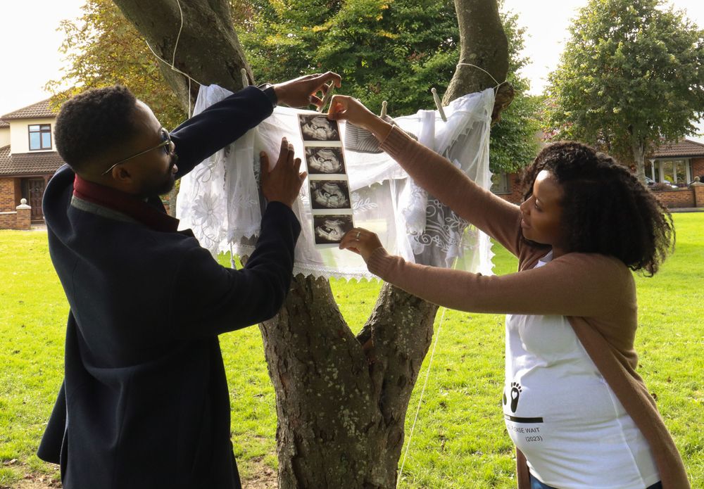 A couple hangs ultrasound photos on a white cloth display outdoors.