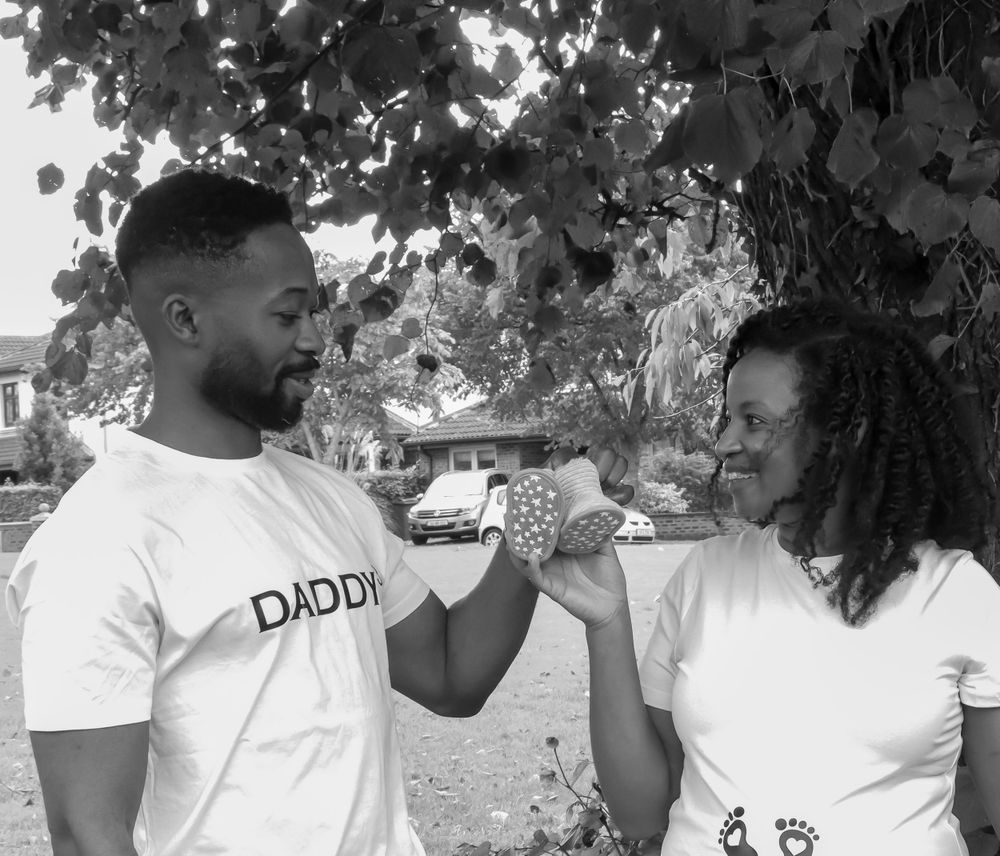 A couple in white t-shirts share a sweet moment outdoors under tree branches.