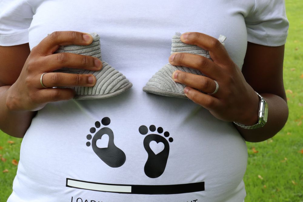 Close-up of hands holding baby socks against a pregnancy countdown shirt with footprints.