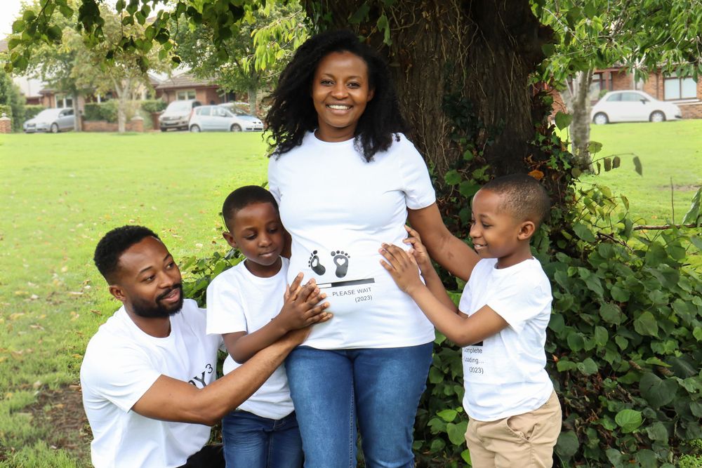 A family wearing matching white t-shirts and jeans laughs together while posing under a tree in a park.