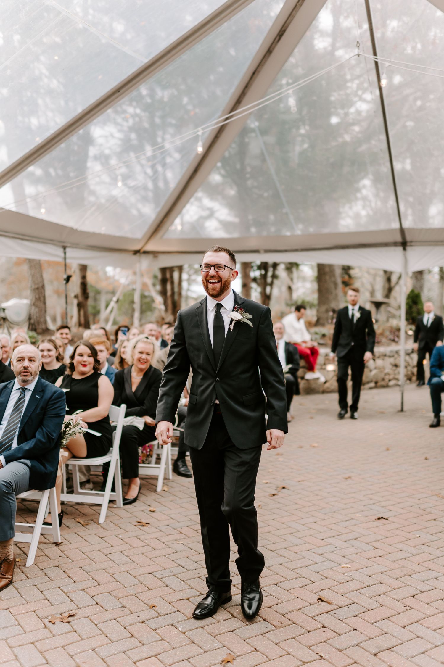 Wedding ceremony setup under a clear tent with guests seated on white chairs.