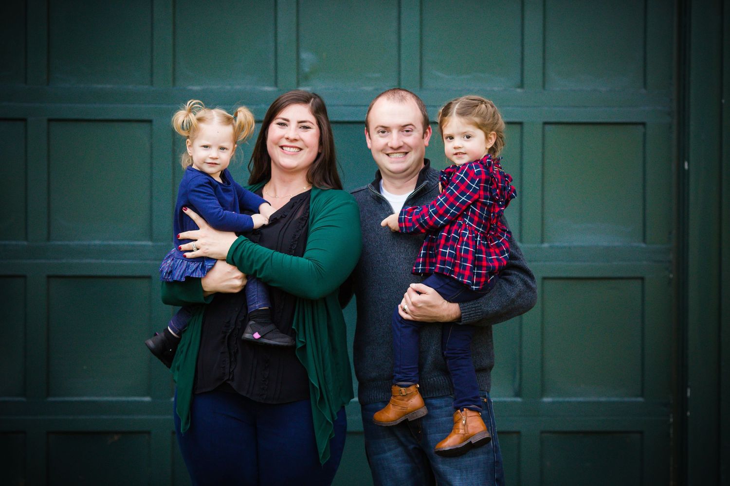 A family poses together against a dark green door wearing coordinated casual outfits.