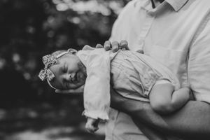 Intimate outdoor photography session showing gentle cradling of a newborn in white attire.