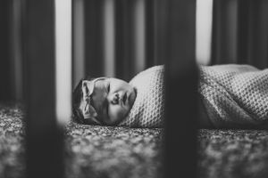 Black and white image of sleeping baby viewed through crib slats.