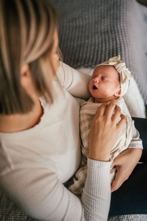 Newborn baby in white wrap yawns while being held.