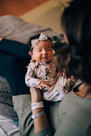 Newborn baby wearing floral outfit resting peacefully on dark bedding.