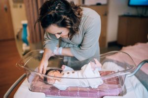 Parent in grey sweater tenderly caring for their newborn baby.