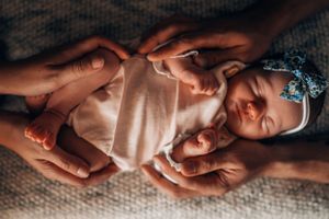 Close-up details of gentle hands holding a sleeping newborn against soft textured fabric.