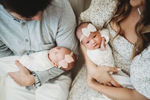 Parents in light colored clothing holding twin newborns dressed in white.