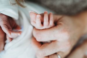 Close-up of gentle hands cradling a newborn baby in white clothing.