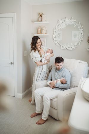 Family portrait in nursery with newborn twins and decorative white mirror.