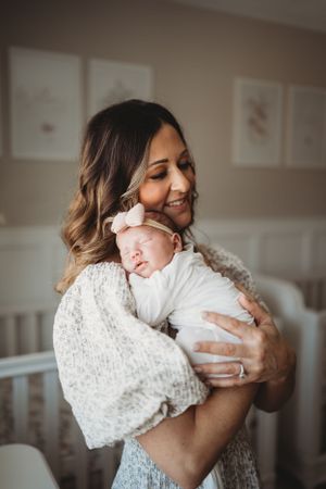 Tender moment between parent and sleeping newborn in white outfit with bow.