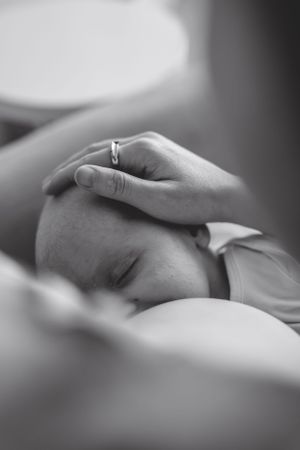 Black and white close-up of a gentle hand touching a newborn's head.