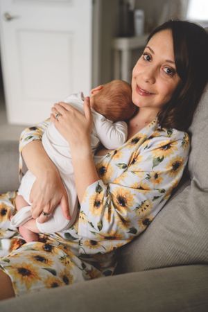 A tender moment between parent and newborn on a grey couch in a sunlit room.