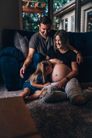 A family shares an intimate moment together on their living room floor while admiring a pregnant belly.