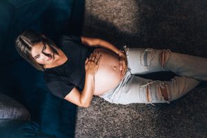 An expectant parent rests on a navy blue couch while cradling their baby bump.