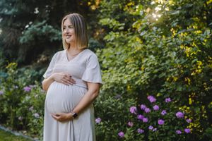 A maternity photo in a garden with purple flowers showing a person in a flowing white dress.
