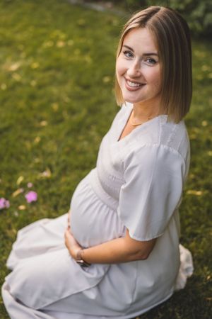 A maternity portrait outdoors with purple flowers and a flowing white dress.