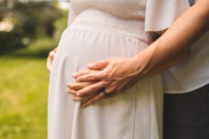 Close-up shot of hands tenderly cradling a pregnant belly in a white dress.