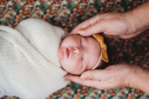 Newborn baby swaddled in white blanket with gentle hands cradling their head.