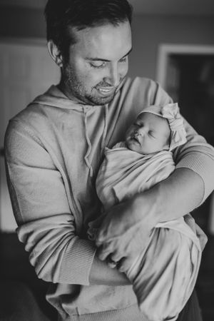 Parent in grey sweater cradles sleeping newborn wrapped in light fabric.