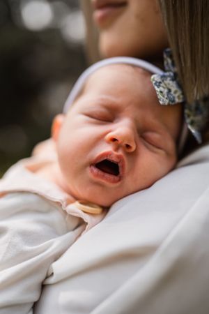 Close up of yawning newborn baby wearing floral bow accessory.