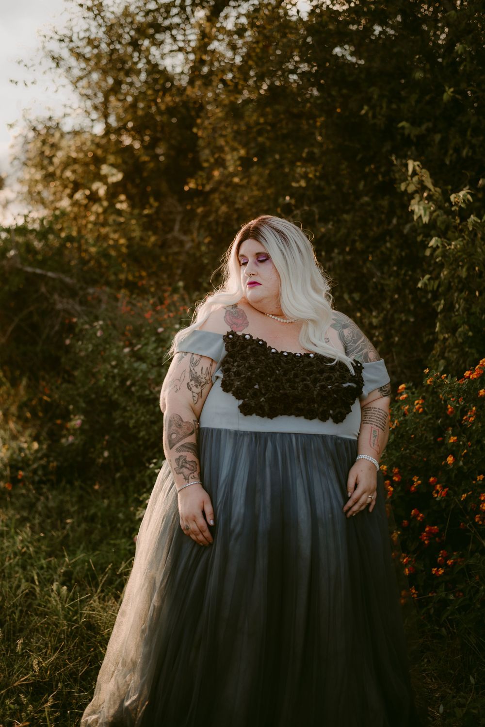 Fashion portrait with a detailed black bodice and flowing blue skirt in a garden setting.