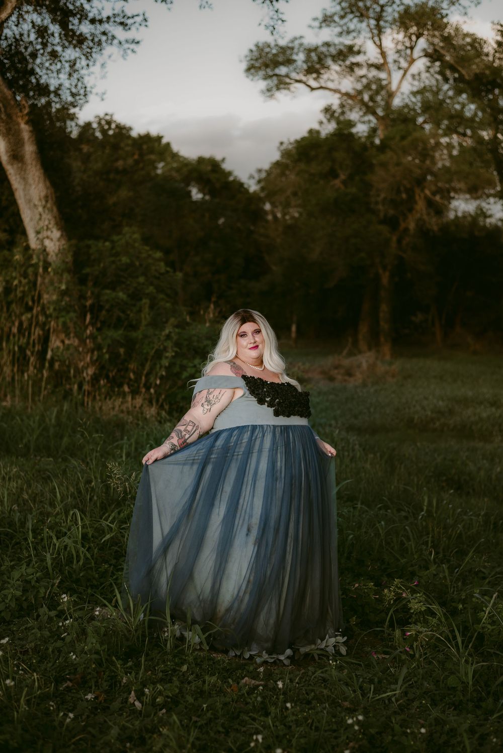 A flowing blue tulle dress photoshoot in a natural woodland setting during golden hour.