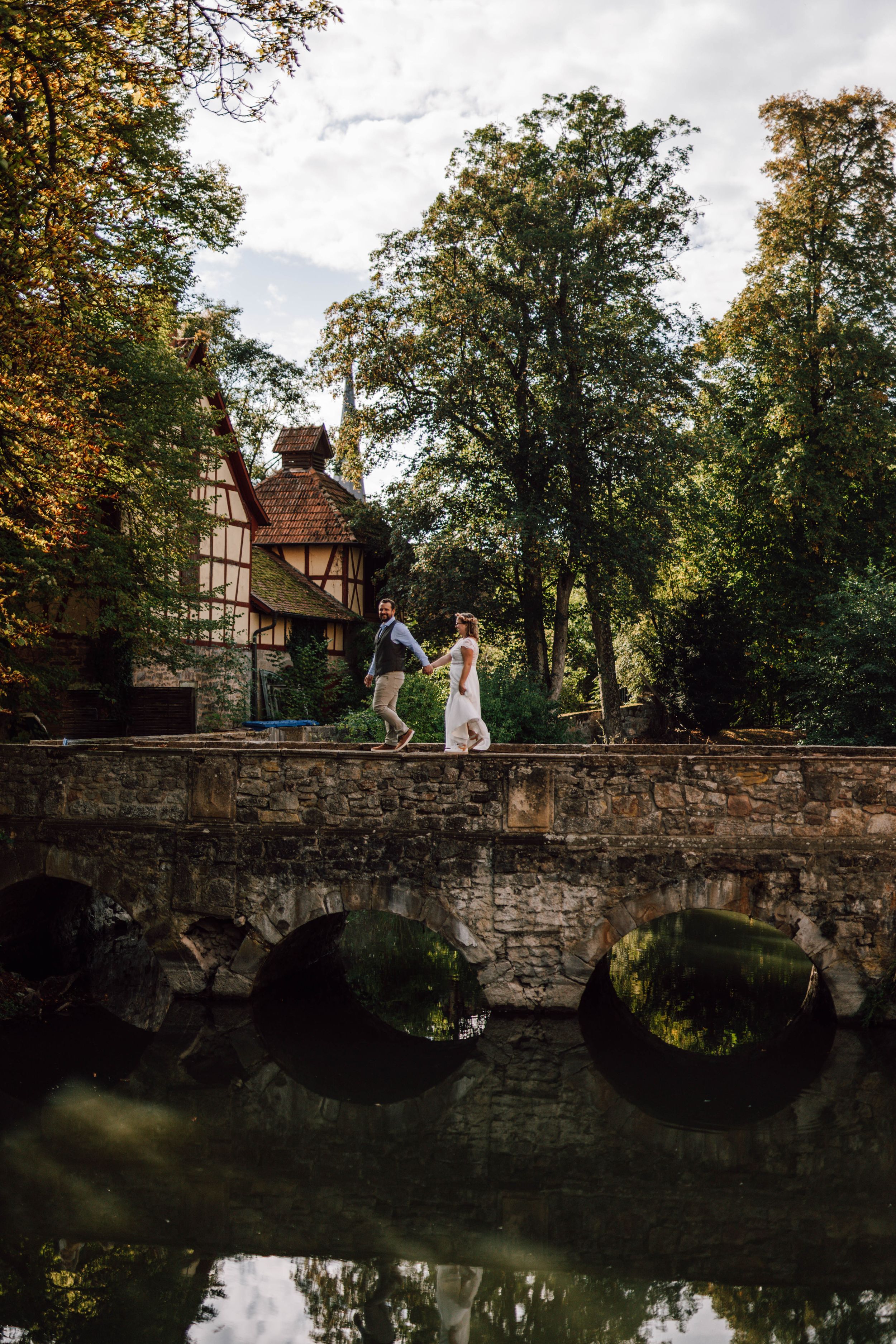 Romantic stone bridge over reflective pond surrounded by autumn trees and historic buildings.